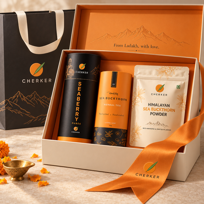 A Cherker gift set containing Seaberry Puree, Himalayan Sea Buckthorn Powder, and Indian Sea Buckthorn Herbal Tea, presented in an open cream-colored box with an orange ribbon, alongside a black branded gift bag on a light stone surface.
